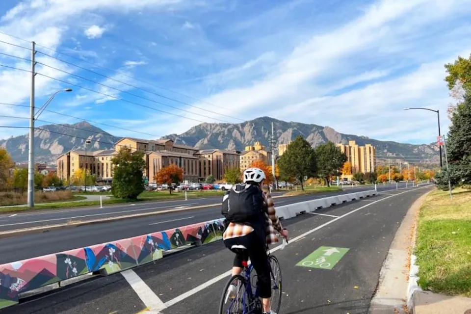 Bike lane in Boulder, Colorado with tall concrete barrier separating it from vehicle lanes and one cyclist passing by.